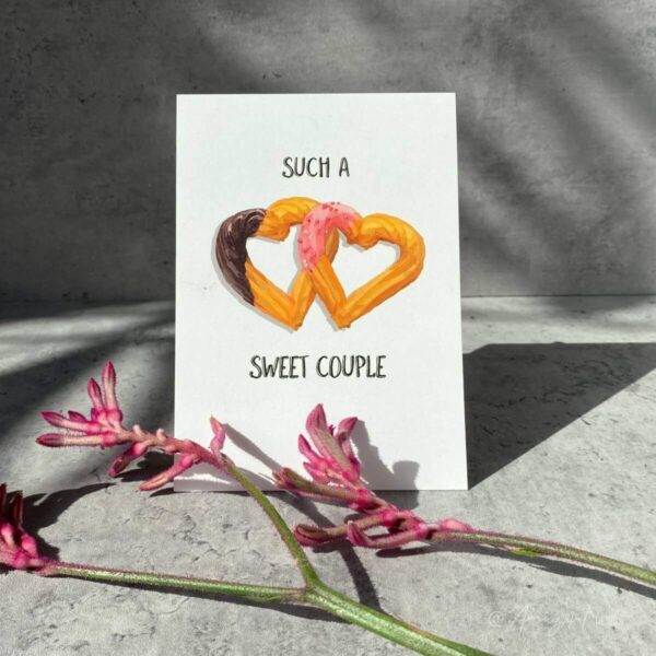Mood image of the "Such a Sweet Couple" AmuzAnt original greeting card. The card has an illustration of 2 heart-shaped churros and is perfect for well wishes for a happy couple.