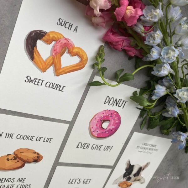 Mood image of several original AmuzAnt greeting cards; one with a pink donut and the text "Donut Ever Give Up", and one with churros and the words: "Such a sweet couple" and several other cookie-themed cards.
